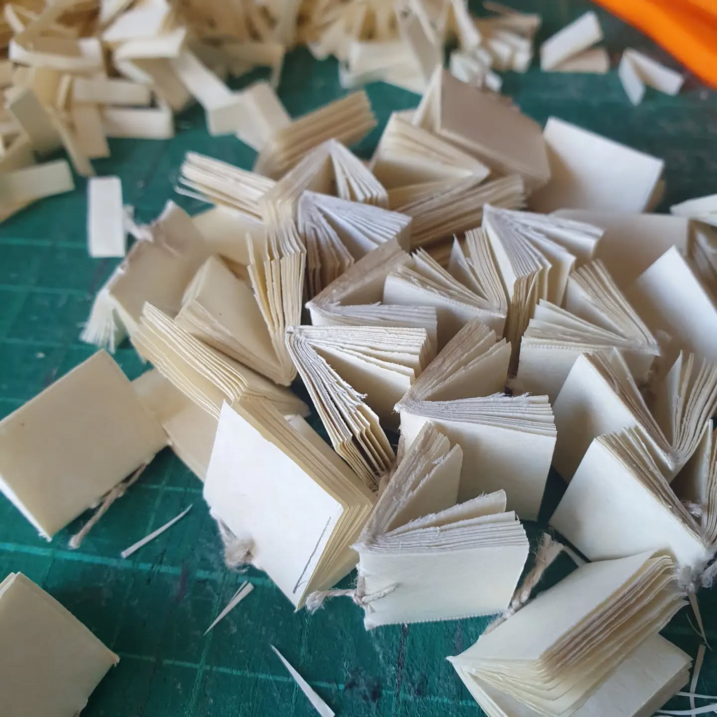 Preparing the tiniest of books for @chethamslibrary medieval fair this Saturday. 

[Image description: a pile of miniature textblocks with offcuts behind them.]