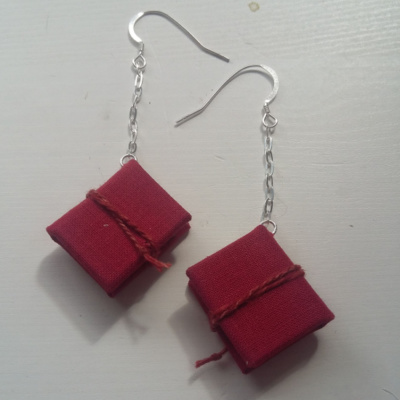 A pair of red miniature books on silver earhooks with a chain drop. They are held shut with a red twisted cord.