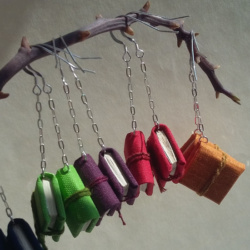 Different colours of book earrings hanging from silver chain from a branch