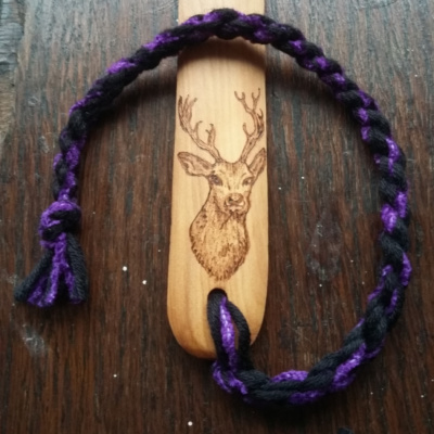 A wooden bonefolder with a stag pyrographed onto it and black and purple twisted cotton tail.