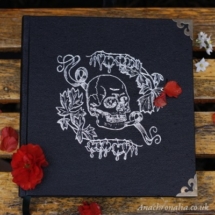 A black book with silver image of a skull and flowers on the cover, and metal corners.