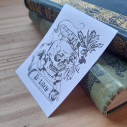 A bookplate featuring a skull lying on a book surrounded by bleeding heart flowers. The words Ex Libris are written on the book.