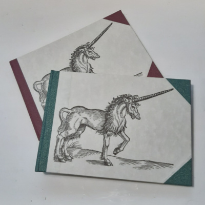 An image of two landscape notebooks with coloured spines and corners and a woodcut of a unicorn on the cover