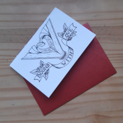 A small pamphlet notebook resting on a red envelope. The notebook features a picture of an open book with pages turned into a heart shape, and a banner surrounded by roses that reads "Bound With Love"