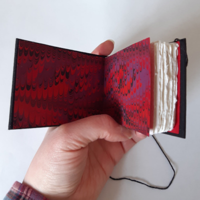 A sketchbook held open to show the red, purple, and black combed end papers