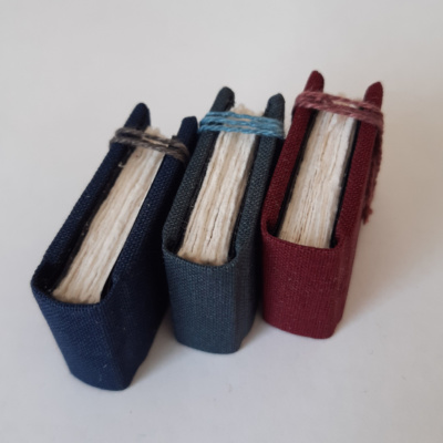 Three miniature books with rough edged text block and linen ties holding them shut.