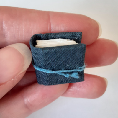 A tiny miniature book in blue grey held in a hand