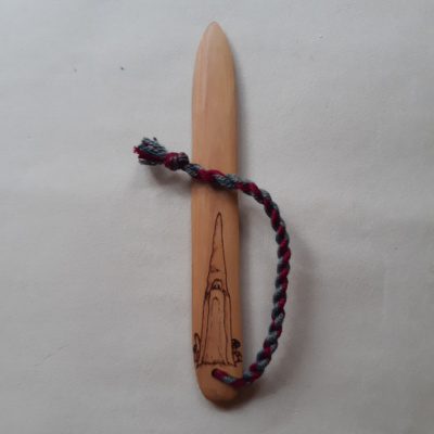 A wooden bonefolder pyrographed with a Scandinavian-style gnome standing among mushrooms
