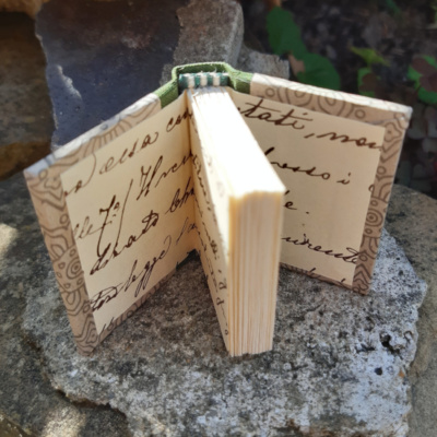 A miniature book opened to show off the endpapers with decorative handwriting on.