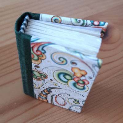 miniature book with green spine and colourful swirl decorated covers