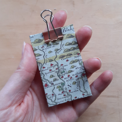 a hand holding a miniature clip board covered in yorkshire map paper and finished with a rose gold clip