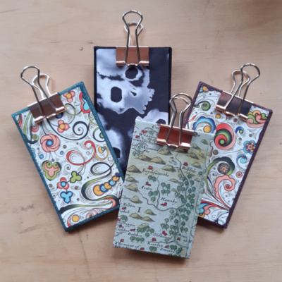 A grouped shot of 4 different designs of clipboards, one with a map image, one swirls with purple, one swirls with green, and one black with white stylised skulls,. They all have rose gold clips.