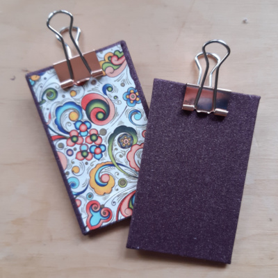 a pair of miniature clipboards showing the purple glitter book cloth and Italian swirl decorative paper. Both have a rose gold clip.
