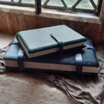 Two medieval-style books, one leather, one velvet, stacked on top of each other, on a windowsilll