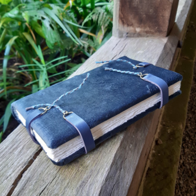 Blue grey velvet book angled to show the two leather clasps across the foredge. A further two are at head and tail and fasten on the front cover with a brass loop and nail.