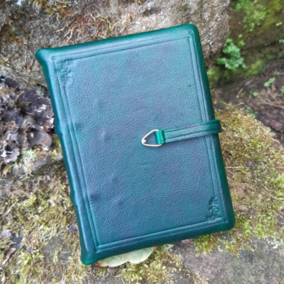 A medieval book covered in dark green leather with blind tooling and a strap that fastens in the centre of the cover..
