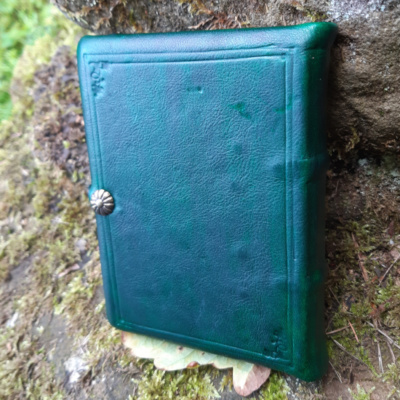 A medieval book covered in dark green leather with blind tooling and a strap.