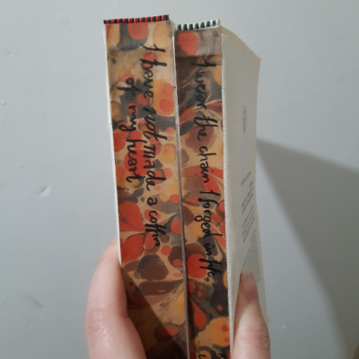 The spines of two textblocks, lined with marbled paper and with a quote from the book written on it.