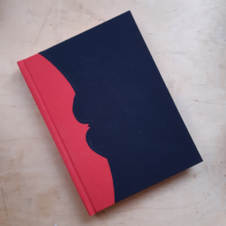A notebook with red spine and black covers where the covers are cut to create a bat silhouette along the spine.
