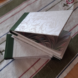 Four notebooks with white shimmery floral textured paper covers and green spines with one open to show its printed marbled endpapers