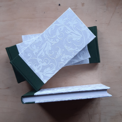 Four notebooks with white shimmery floral textured paper covers and green spines with one from above to show its white pages