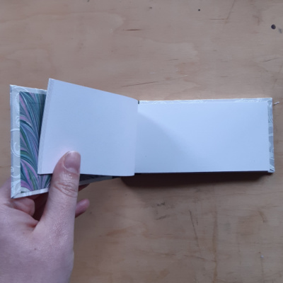 A hand holding open a landscape format book open to show off the blank book pages.