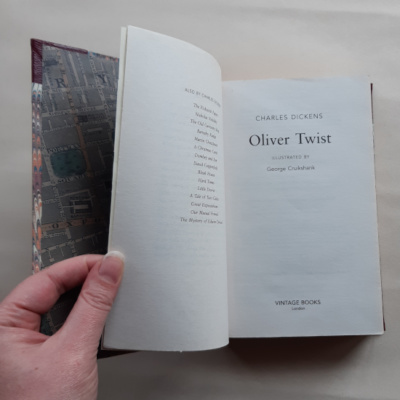 A hand holding a book open to the frontispeice for Oliver Twist by Charles Dickens
