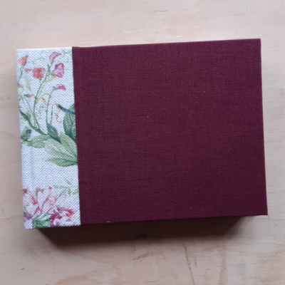 A wine red book with watercolour style floral fabric spine.
