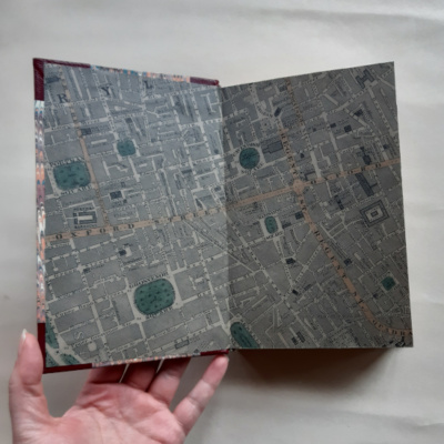 A hand holding a book open to show the endpapers which feature an 1860s map of London.
