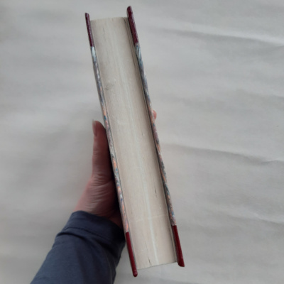 A hand holding a book with the foredge out to show the worn edges of the aged paper.