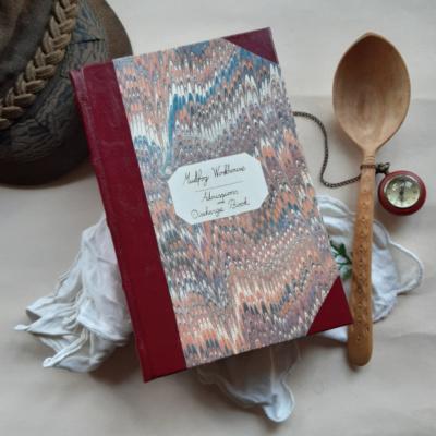 A book styled to look like a vintage workhouse ledger, surrounded by handkerchiefs, a hat, pocket watch and a wooden spoon.