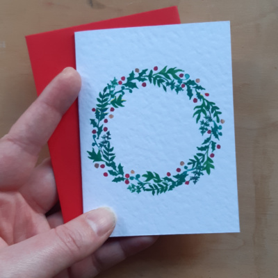 A wreath card with envelope held in a hand