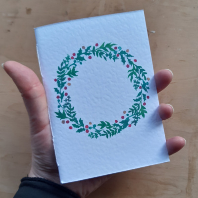 A hand holding a pamphlet with a wreath on