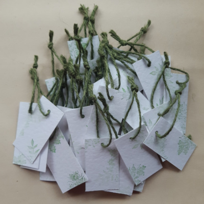 A pile of gift tags of white hammered card with foliage detail stamped on and finished with a green just twine