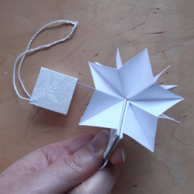 A square book with white covers held open so the pages make the shape of a star..