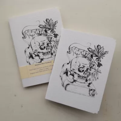 Two white hammered card covered pamphlets on a cream background. The cover images are of a skull resting on a book with a spray of bleeding hearts and a ribbon arching above it.