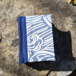 A miniature book with a blue cloth spine and blue and white wave patterned covers