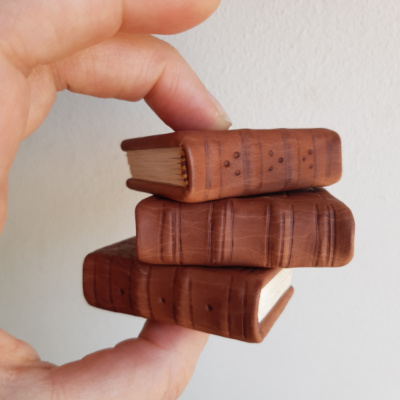A hand holding a stack of three miniature books, showing off the spines which are blind tooled with a series of lines and dots.