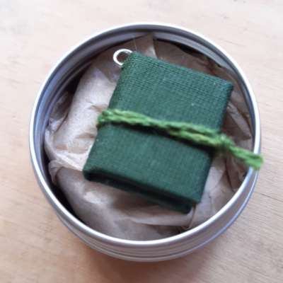 A green miniature book inside a metal gift tin.