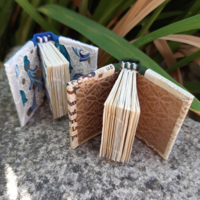 Two miniature books open to show off blue florentine end papers, and brass chyogami endpapers.