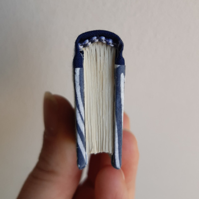 A miniature book photographed from above to show the curved blue spine and the blue and white stick on headbands