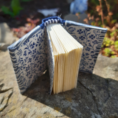 A miniature book open to show off the blue foliage and flower on white paper endpapers.