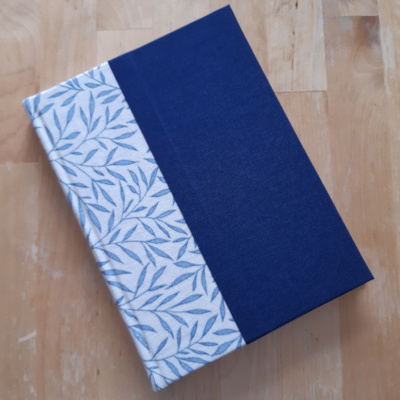 An A5 book with a cream and blue foliage fabric on the spine and dark blue cloth covers.