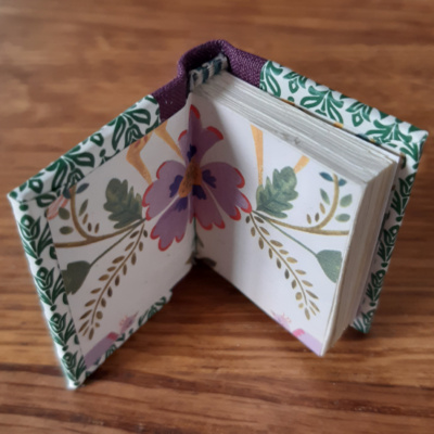 A miniature book open to show the floral end paper with purple flower
