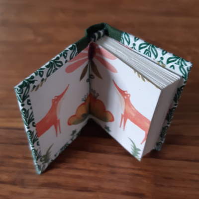 A miniature book open to show the partial image of two foxes on the endpapers