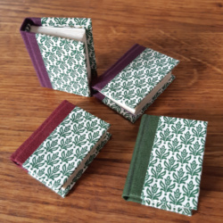 Four miniature books with stylised floral paper covers and book cloth covered spines, in red, green, and purple.