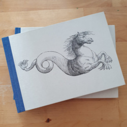 A landscape A5 hardback notebook with blue spine and an image of a horse with a curving fish tail on the parchment paper cover