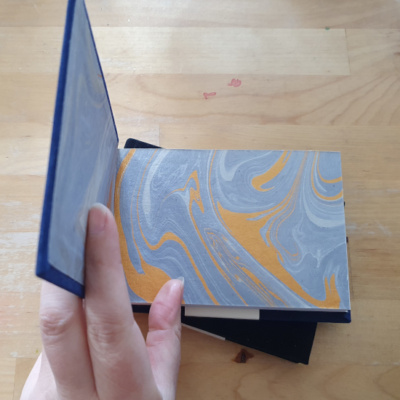 a hand holding a book open to show grey and gold swirled marbled end papers.
