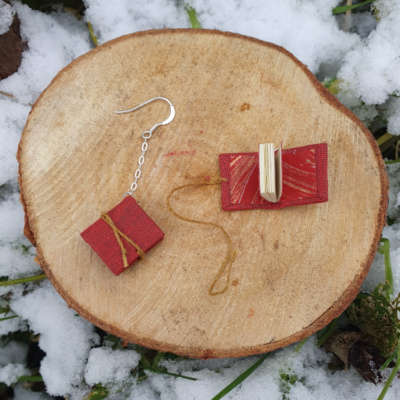 A pair of red miniature books with golden yellow ties, are hung from silver ear hooks and chain. One is open to show off the gold and red hand-marbled endpapers.