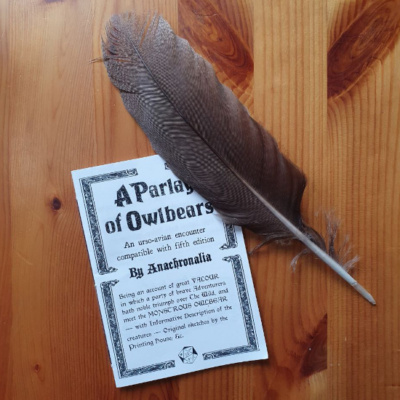 A handbound pamphlet titled A Parlay of Owlbears on a wooden background with an owl feather.